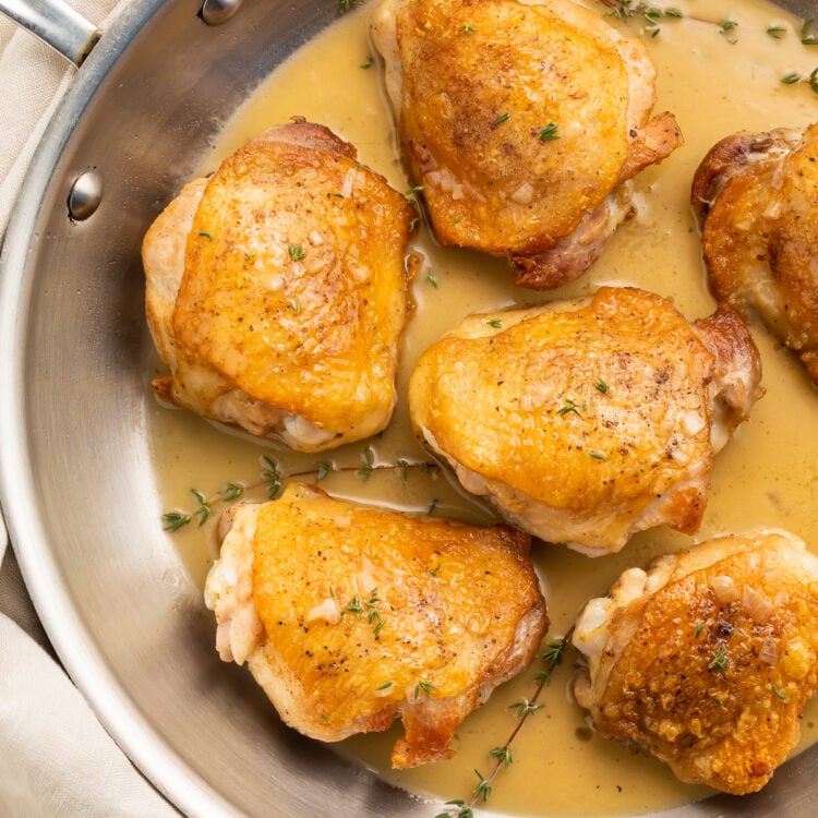 Pan-seared chicken thighs in a simple pan sauce, resting in a silver saucepan.