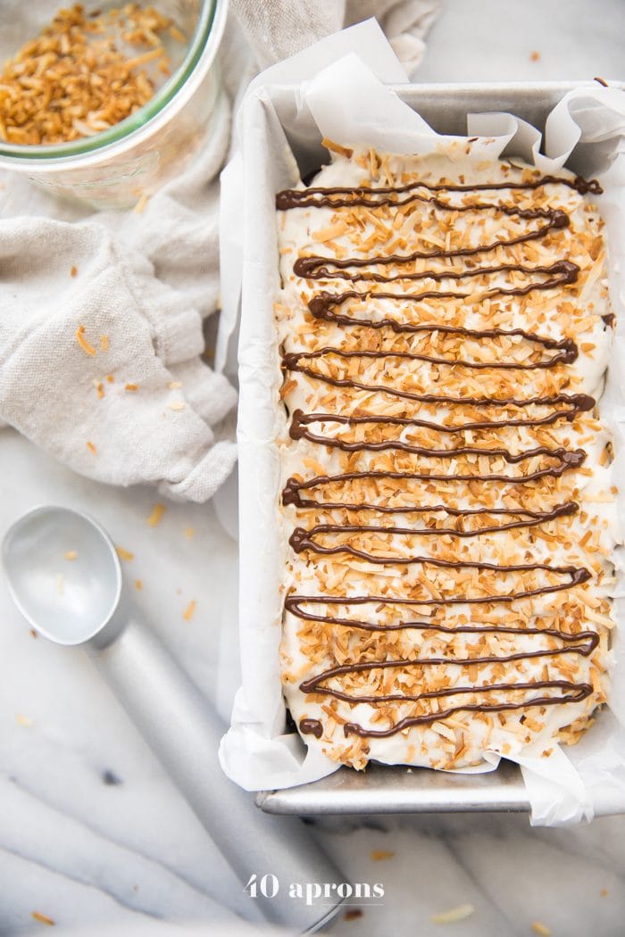 Container of Samoas cookies ice cream recipe topped with toasted coconut and chocolate drizzle