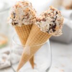 Samoas cookies ice cream in two cones in a glass with ice cream container in the background
