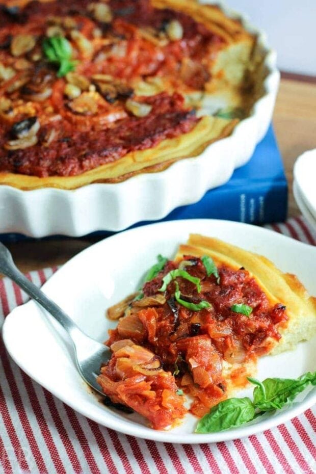 a slice of Whole30 Tomato Tart on a small white plate with the tart dish in the background.