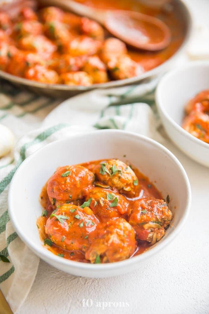 Italian Whole30 meatballs in creamy tomato sauce in a bowl with skillet in background
