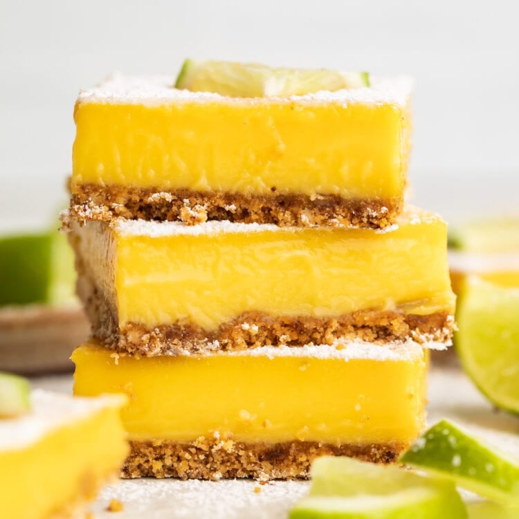 Three square paleo lime bars stacked on top of each other, garnished with powdered sugar and a lime wedge.