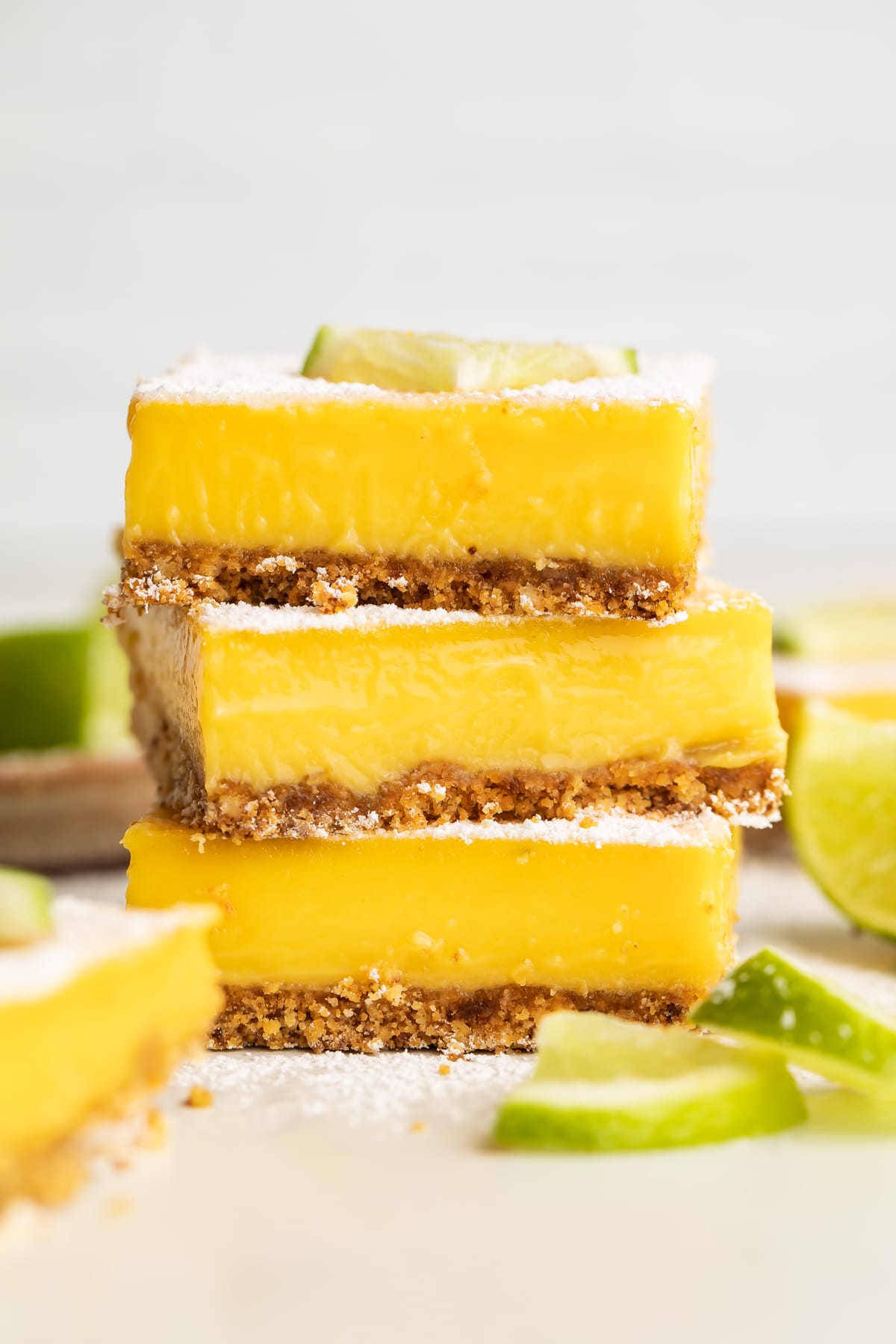 Three square paleo lime bars stacked on top of each other, garnished with powdered sugar and a lime wedge.