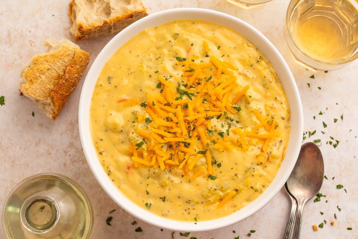 Creamy yellow broccoli cheese soup in white bowl topped with shredded cheese and parsley