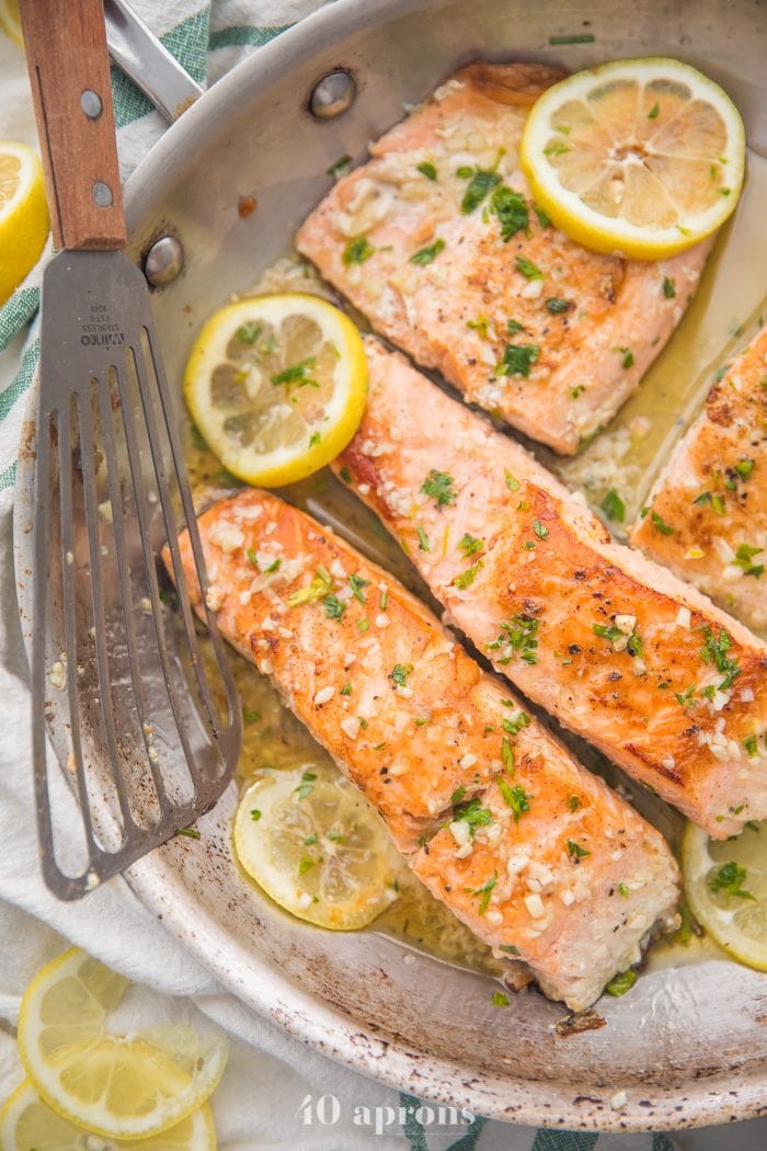 Lemon garlic salmon in a skillet with lemon slices and fish turner