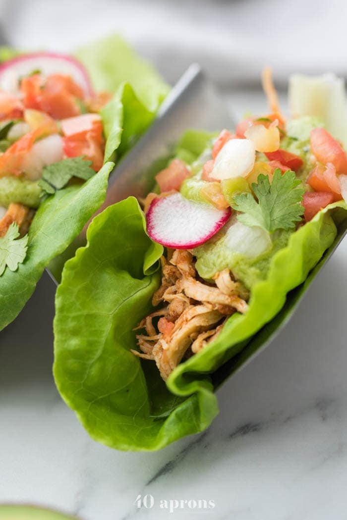 Closeup shot of paleo chicken tacos in lettuce wraps with avocado crema, pico de gallo, and radish slice