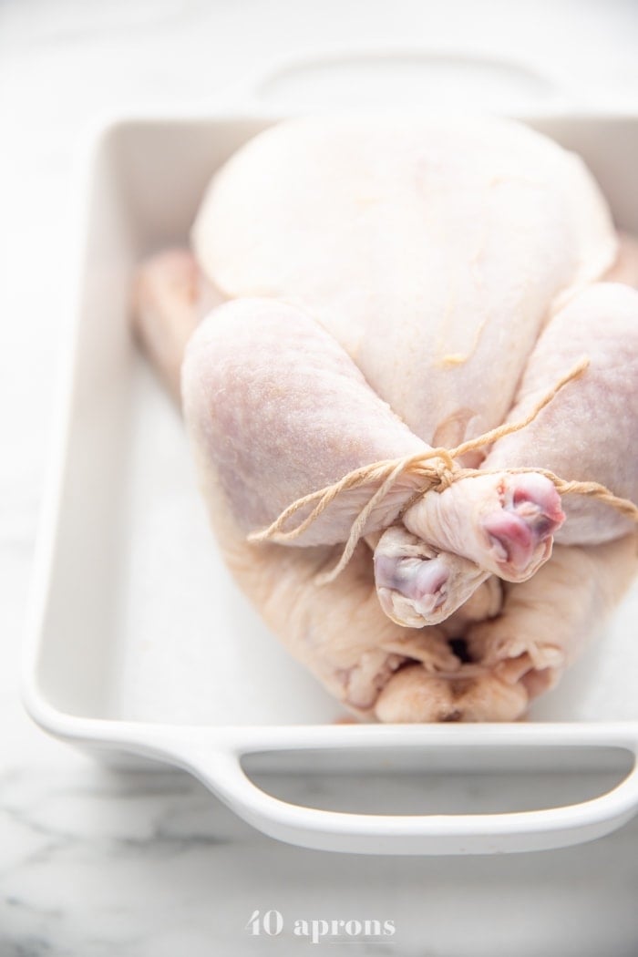 Chicken trussed in white baking dish