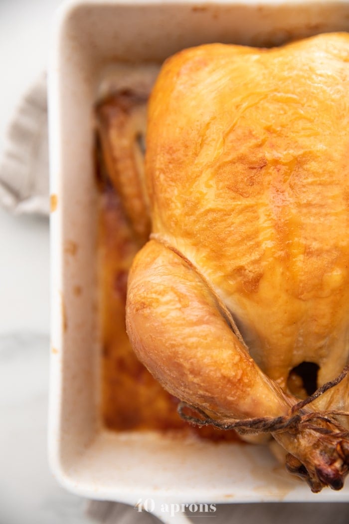 Best easy roast chicken with golden brown skin trussed in a white baking dish