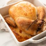 Best easy roast chicken with golden brown skin trussed in a white baking dish