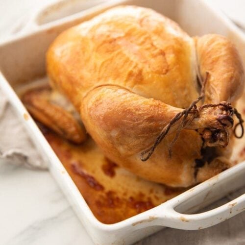 Best easy roast chicken with golden brown skin trussed in a white baking dish