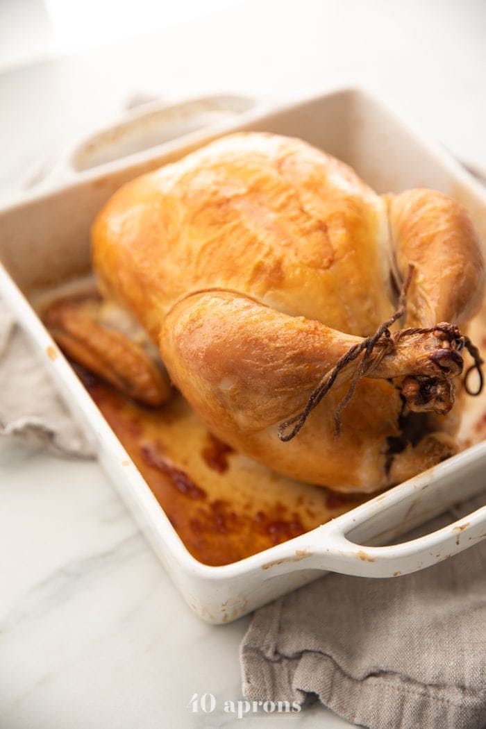 Best easy roast chicken with golden brown skin trussed in a white baking dish