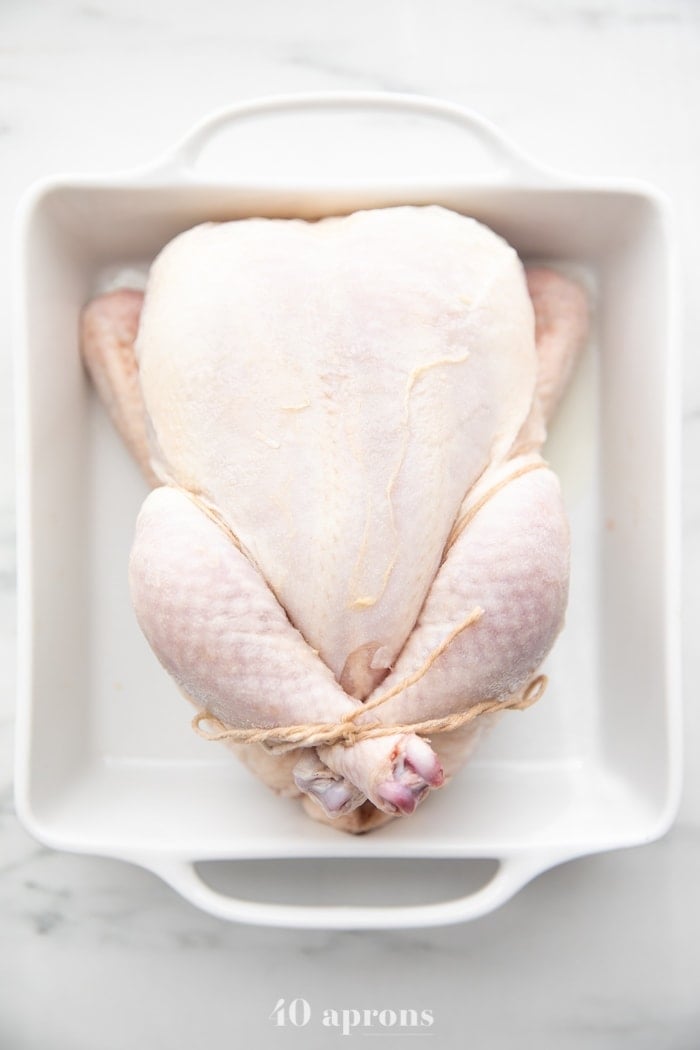 Chicken trussed in white baking dish