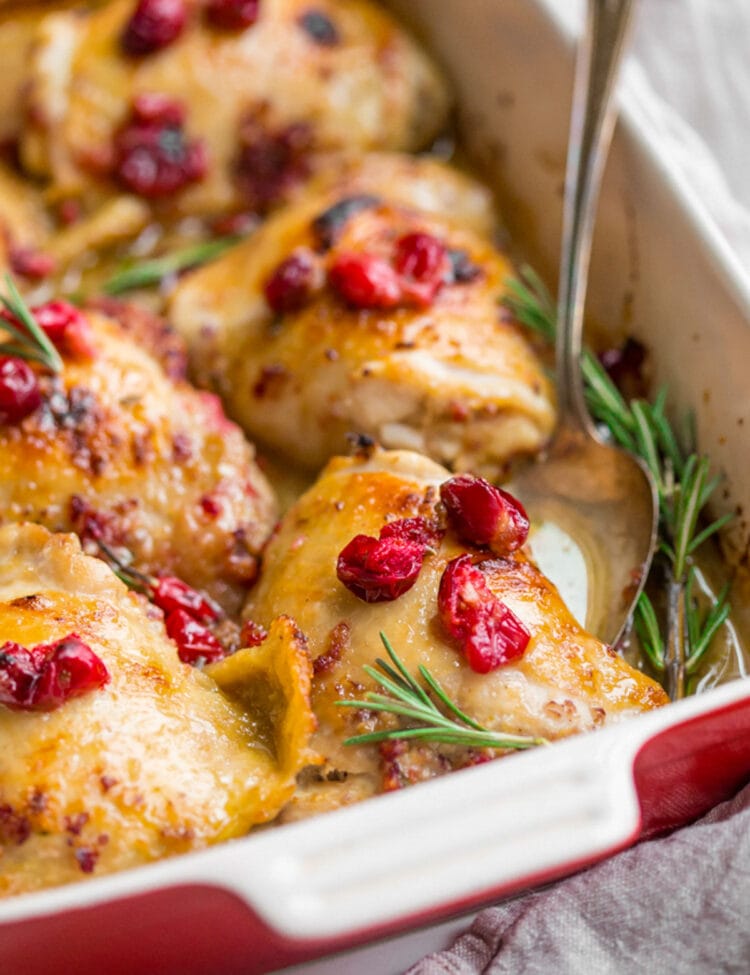 Cranberry rosemary chicken thighs in a red and cream baking dish.