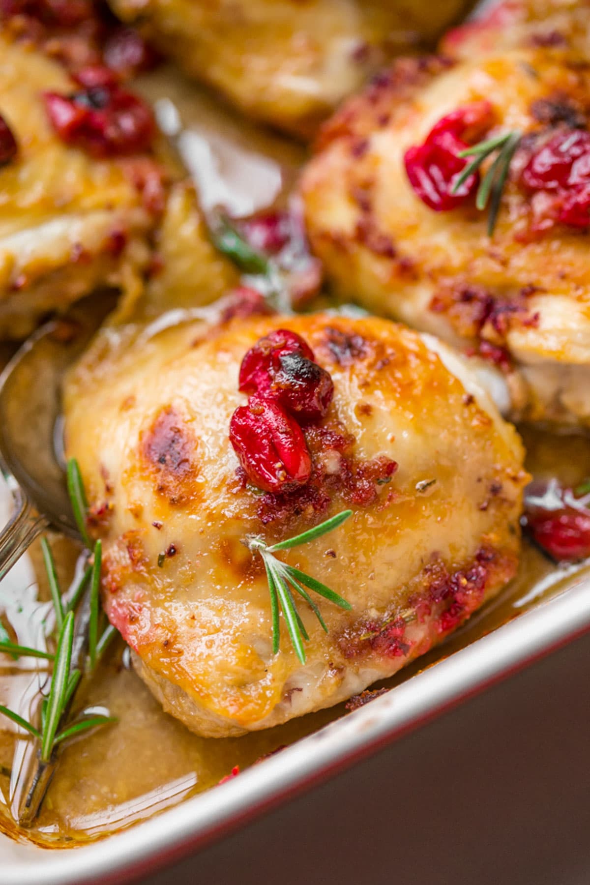 Cranberry rosemary chicken thighs in a red and cream baking dish.