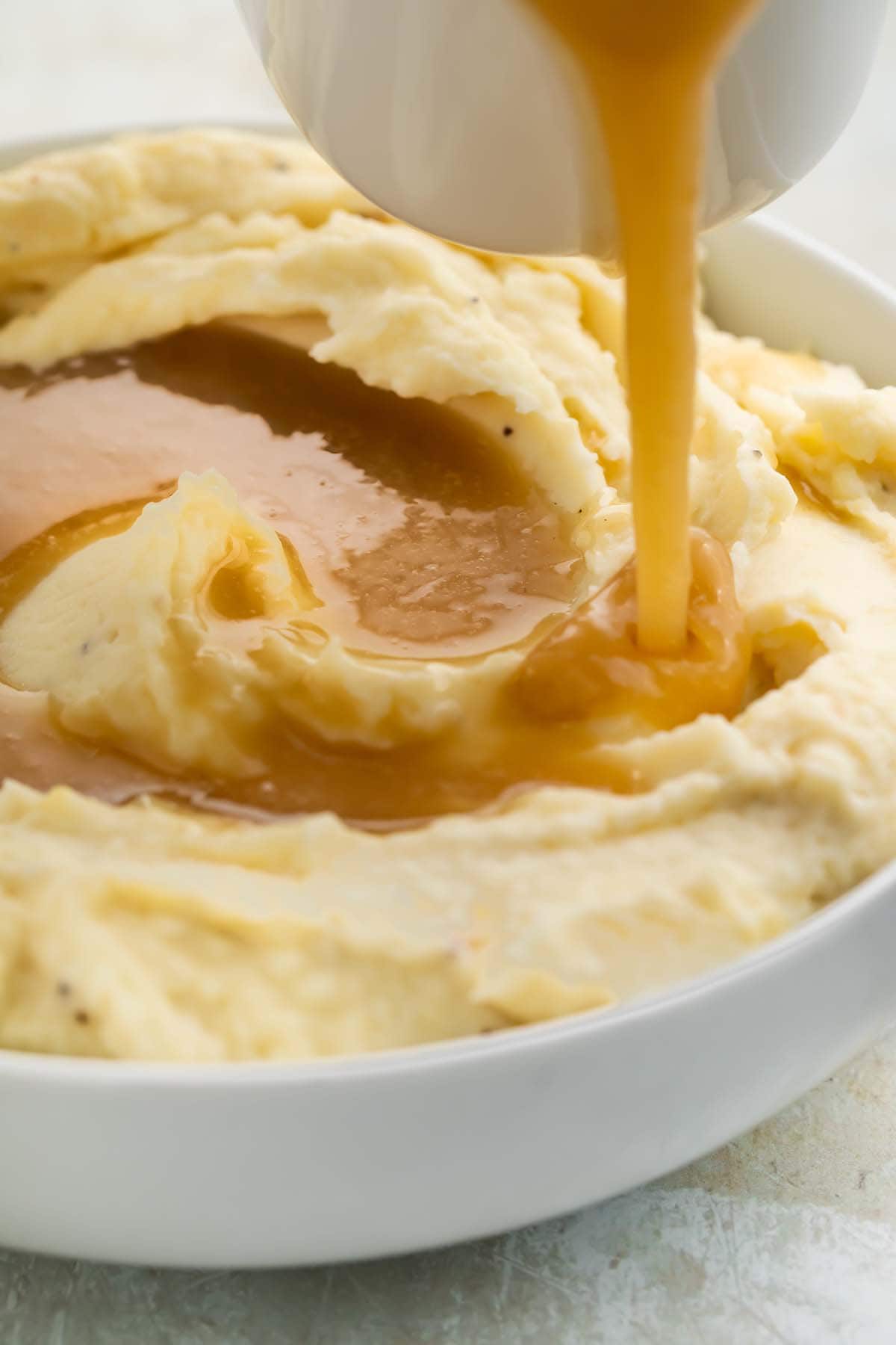 Paleo gravy being poured over a bowl of creamy mashed potatoes.