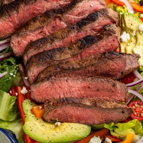 Close-up of a fajita steak salad arranged on a blue and white platter with lime wedges and slices of avocado.