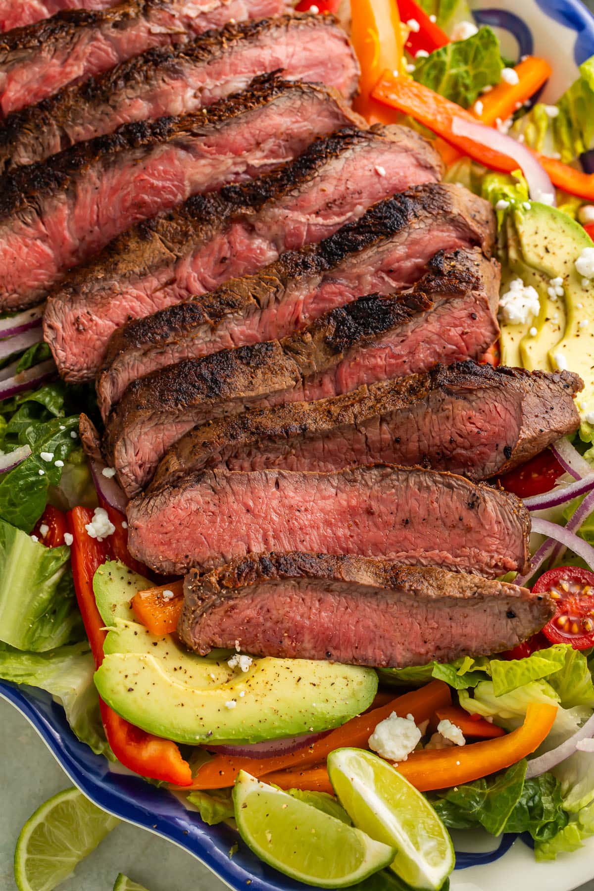 Close-up of a fajita steak salad arranged on a blue and white platter with lime wedges and slices of avocado.