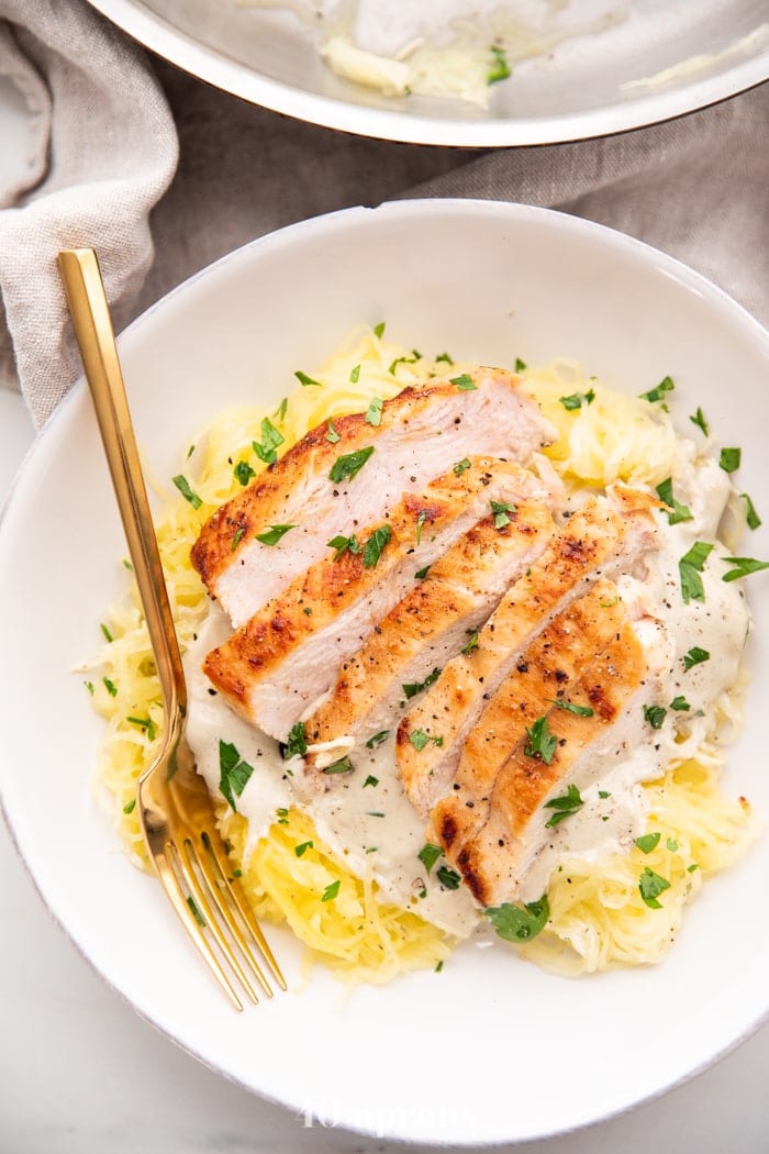 Healthy Whole30 chicken alfredo with spaghetti squash in a white bowl with a gold fork topped with parsley