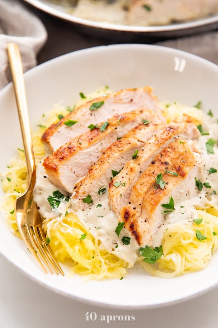 Healthy Whole30 chicken alfredo in a white bowl with gold fork and parsley garnish