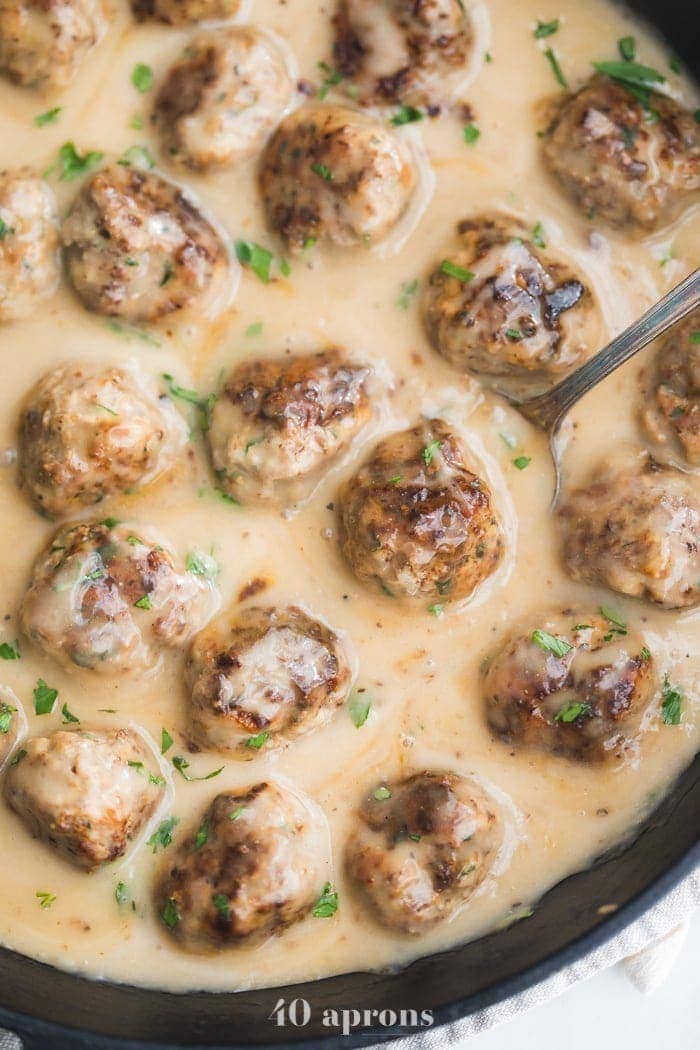 Closeup of Paleo Swedish meatballs in creamy Swedish meatballs sauce in a cast iron skillet overhead