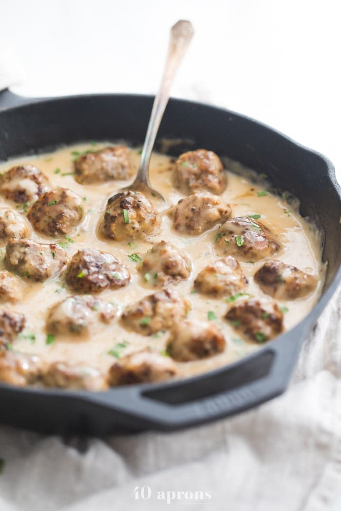 Paleo Swedish meatballs in creamy Swedish meatballs sauce in a cast iron skillet with a spoon