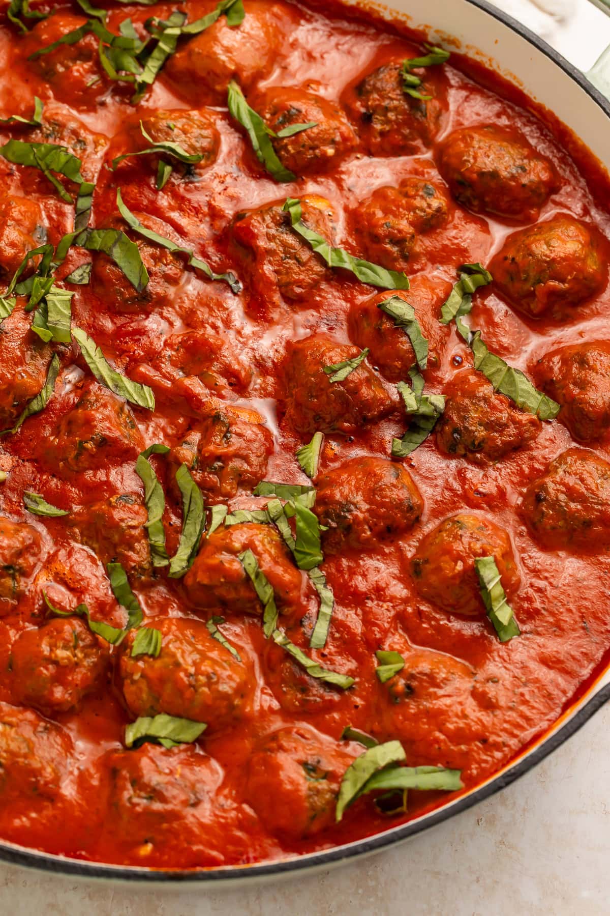 Italian paleo meatballs in creamy red tomato sauce in a large white skillet, garnished with fresh basil ribbons.