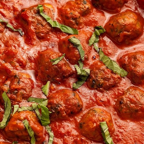 Close-up of Whole30 Italian meatballs in creamy tomato sauce, showing texture and fresh basil garnish.