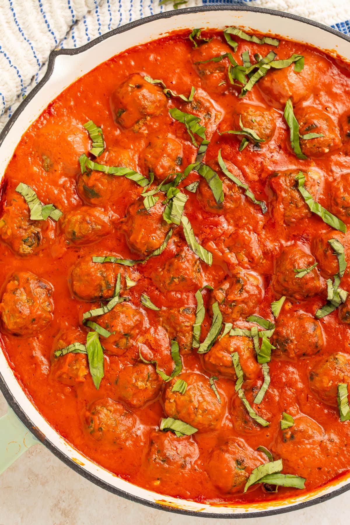 Macro shot of a single Italian meatball in creamy red sauce with basil, showing tender texture.