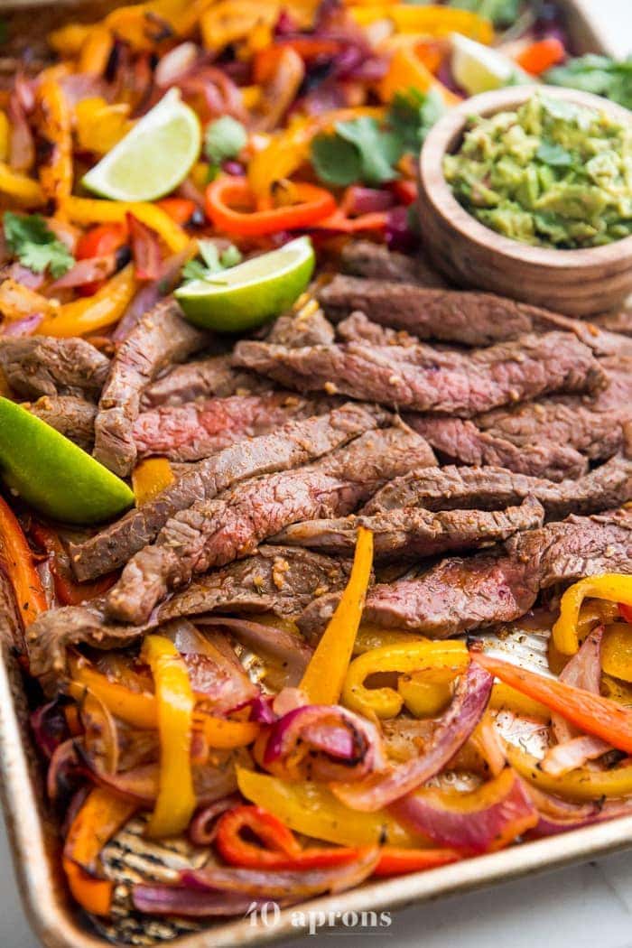 Best sheet pan fajitas with steak and peppers on a sheet pan with lime slices and guacamole off to the side
