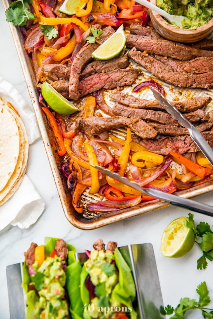 Best sheet pan fajitas with steak and peppers on a sheet pan with lime slices and guacamole off to the side