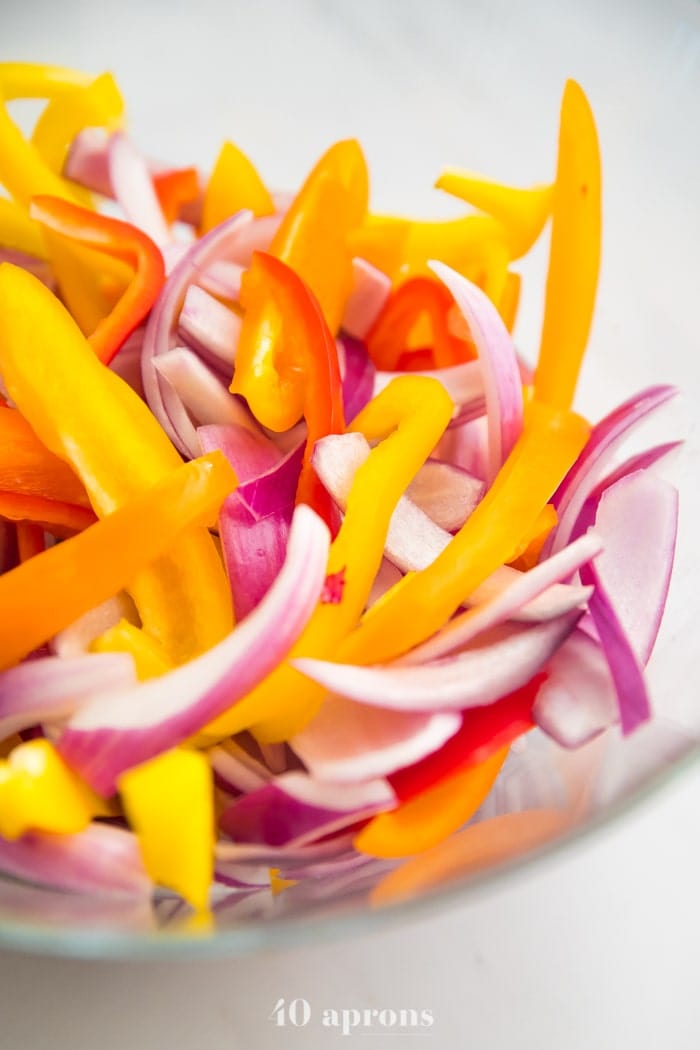 Sliced bell peppers and red onions in a bowl