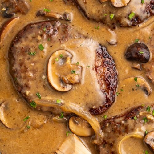 Whole30 salisbury steak in a cast-iron skillet with plenty of brown gravy, mushrooms, and a wooden spoon.