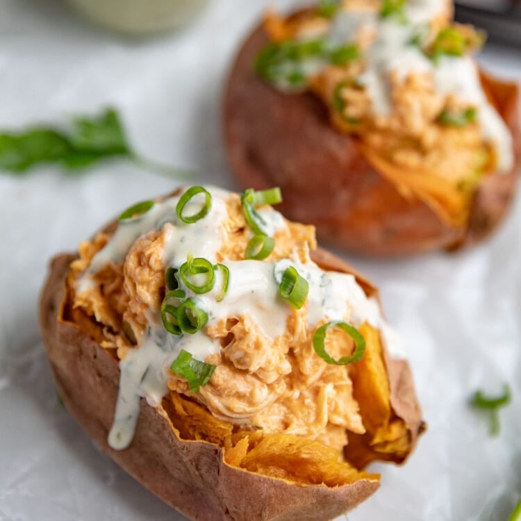 Buffalo chicken stuffed sweet potatoes topped with ranch dressing and green onions.