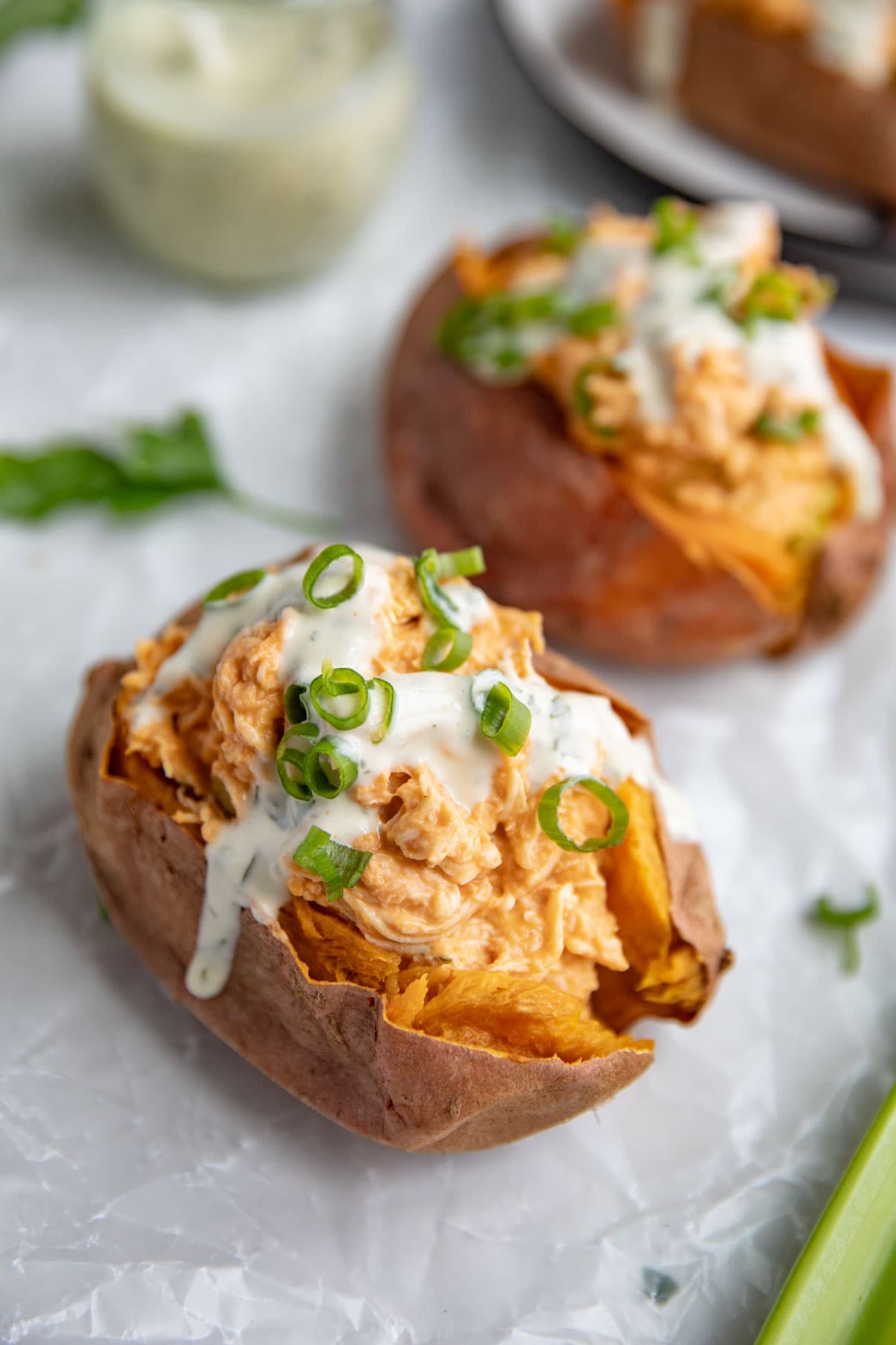 Buffalo chicken stuffed sweet potatoes topped with ranch dressing and green onions.