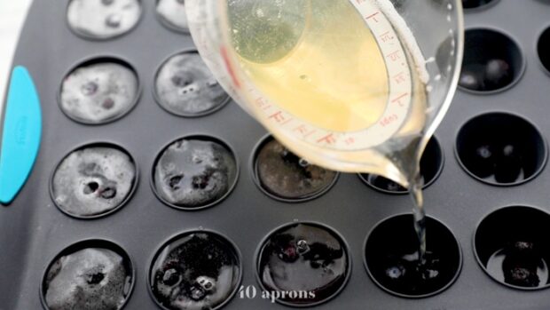 Gelatin-champagne mixture being poured into a silicone muffin pan.