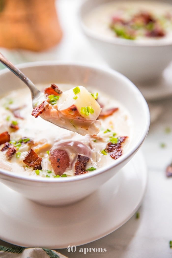 Close up of a spoonful of healthy creamy Whole30 clam chowder in a bowl with bacon and chives