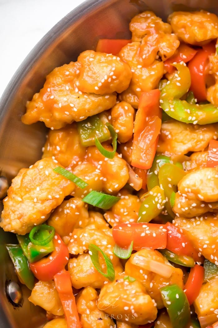 A skillet of healthy sweet and sour chicken with red and green bell peppers