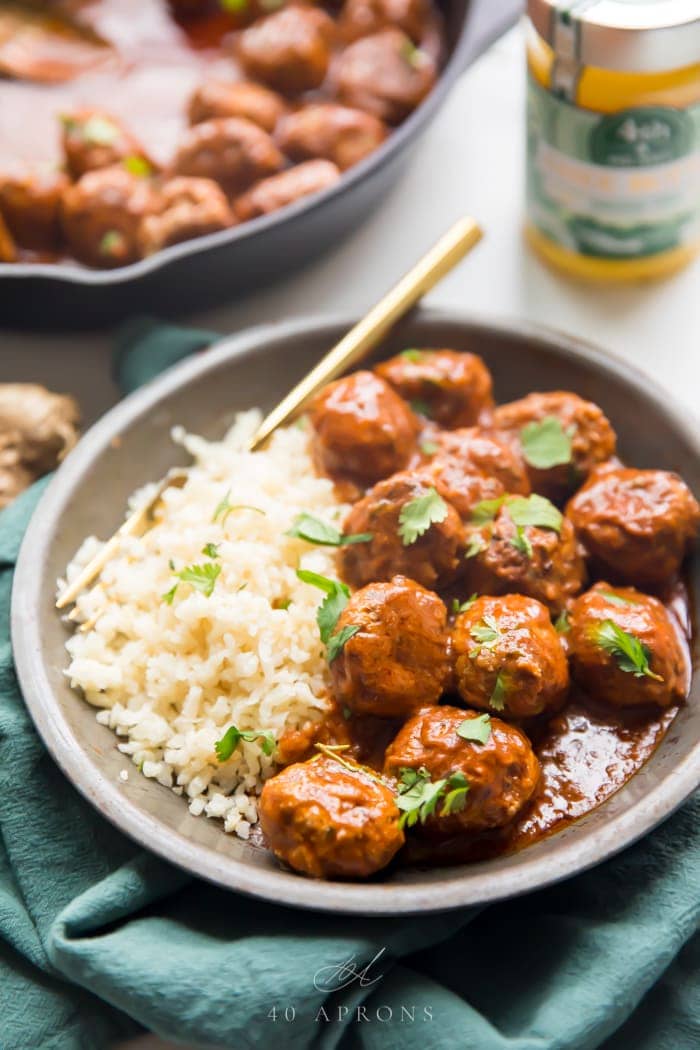 Indian meatballs with creamy sauce next to cauliflower rice topped with cilantro in a grey dish on a green napkin with 4th & Heart Ghee in background