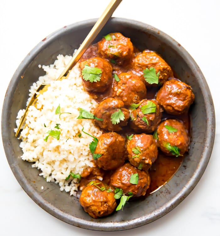 Indian meatballs with creamy sauce next to cauliflower rice topped with cilantro in a grey dish
