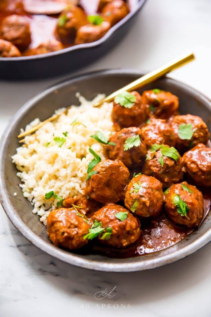 Indian meatballs with creamy sauce next to cauliflower rice topped with cilantro in a grey dish