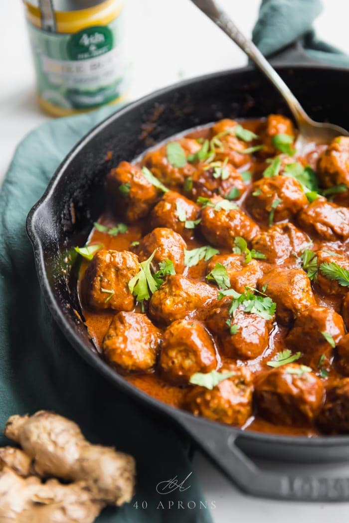 Indian meatballs with creamy sauce next to cauliflower rice topped with cilantro in a cast iron skillet on a green napkin