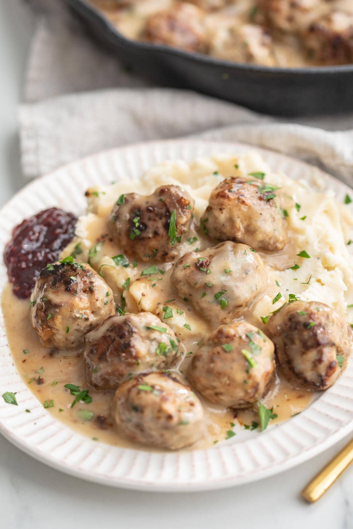 A plate of Whole30 Swedish meatballs and gravy atop a bed of mashed potatoes.