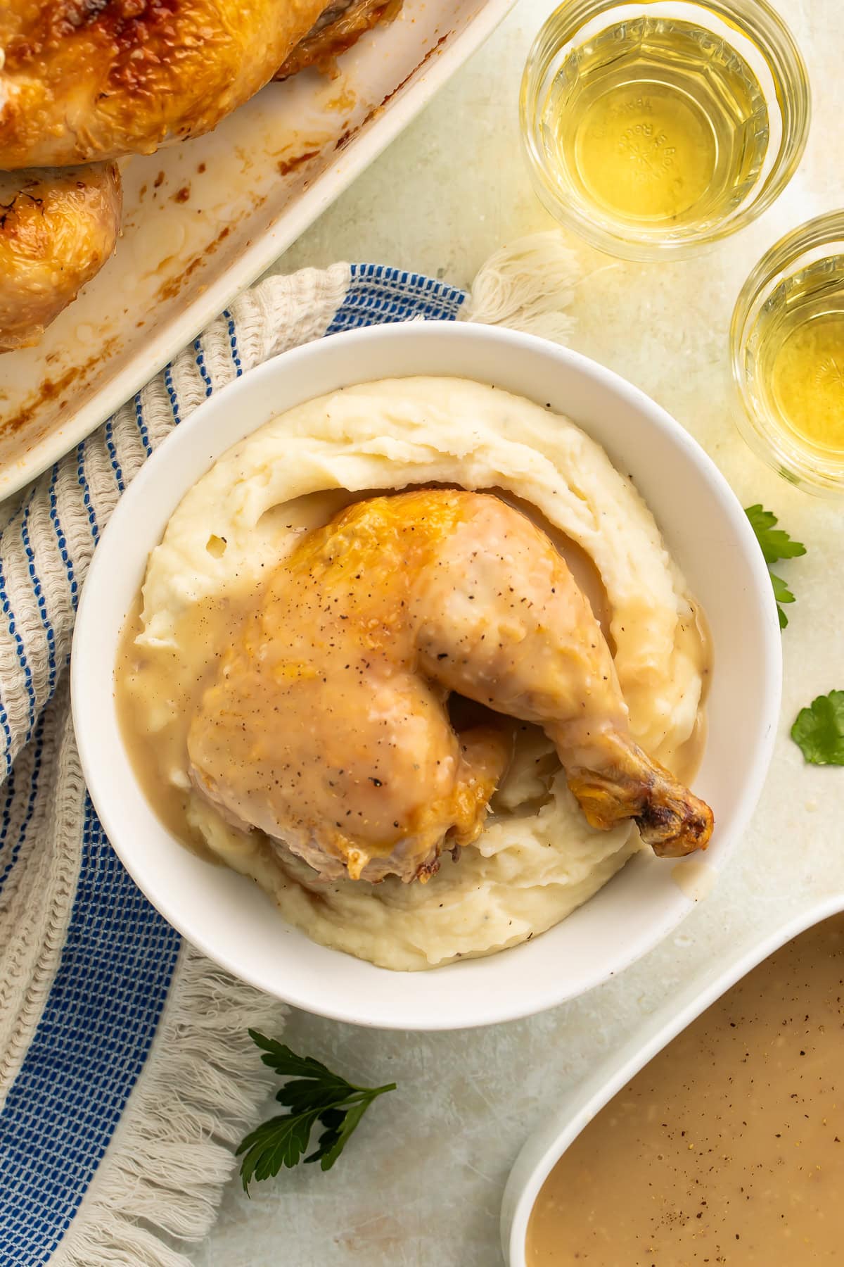 Golden roasted chicken leg and thigh with crispy skin on mashed potatoes in white bowl with gravy