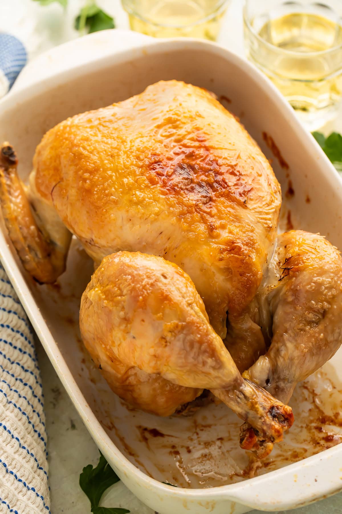 Whole roasted chicken with golden-brown crispy skin in white ceramic baking dish