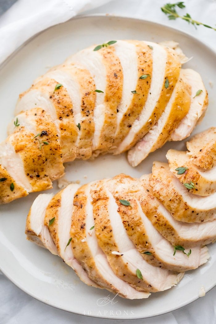 Two Sous vide boneless skinless chicken breasts in slices on a plate with thyme garnish