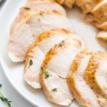 Sous vide boneless skinless chicken breast in slices on a plate with thyme garnish