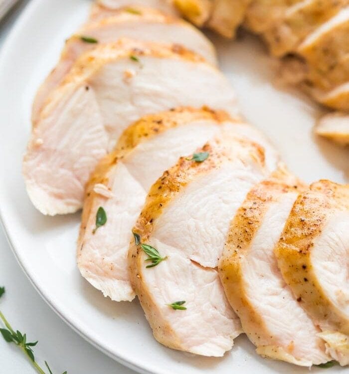 Sous vide boneless skinless chicken breast in slices on a plate with thyme garnish