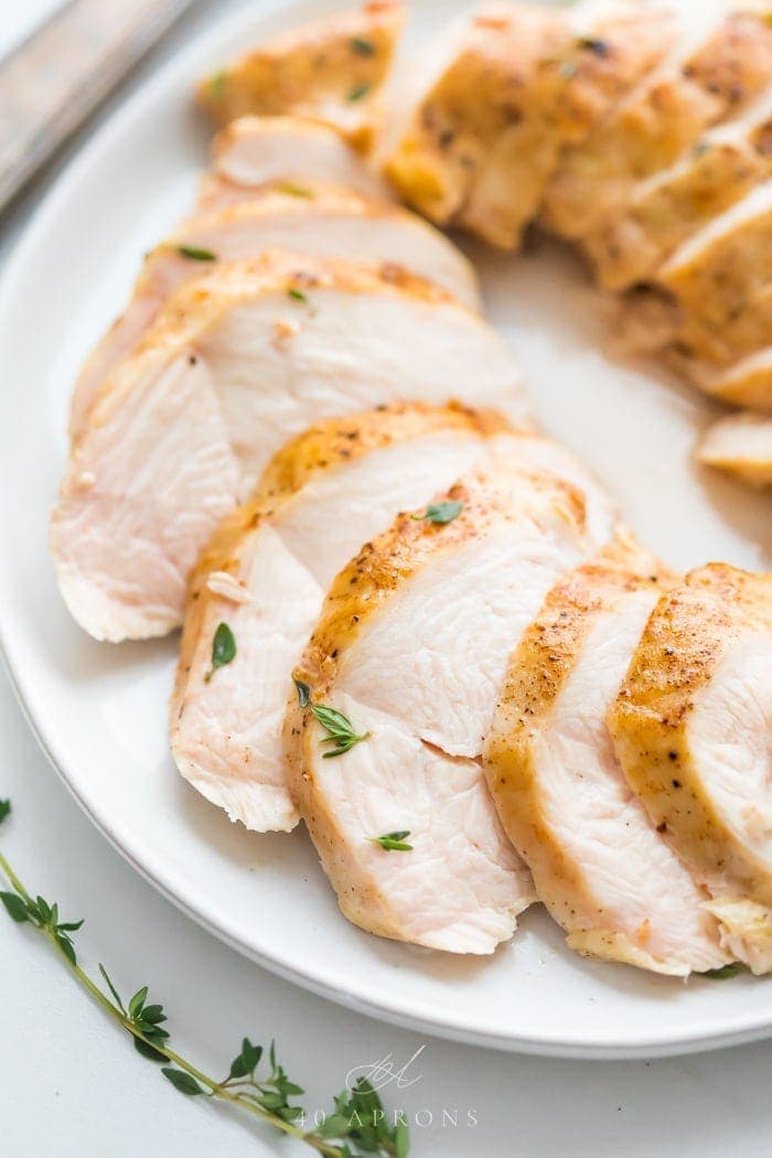 Sous vide boneless skinless chicken breast in slices on a plate with thyme garnish