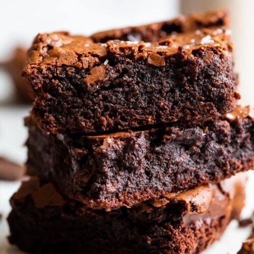 A stack of three paleo brownies showing how fudgy and rich they are, with a crackly top and flake sea salt on top