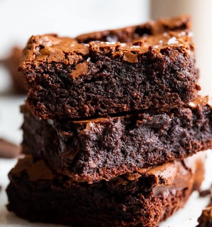 A stack of three paleo brownies showing how fudgy and rich they are, with a crackly top and flake sea salt on top